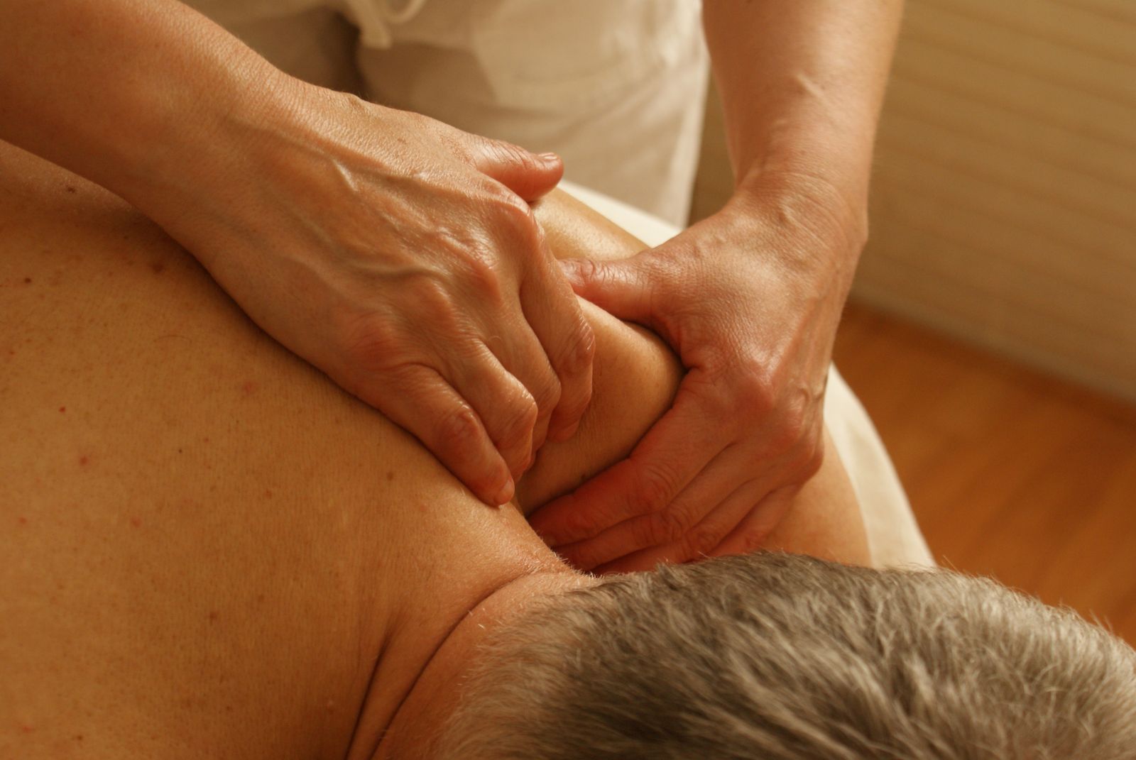 Close-up of a therapist applying focused thumb pressure to a client's shoulder during a deep tissue massage